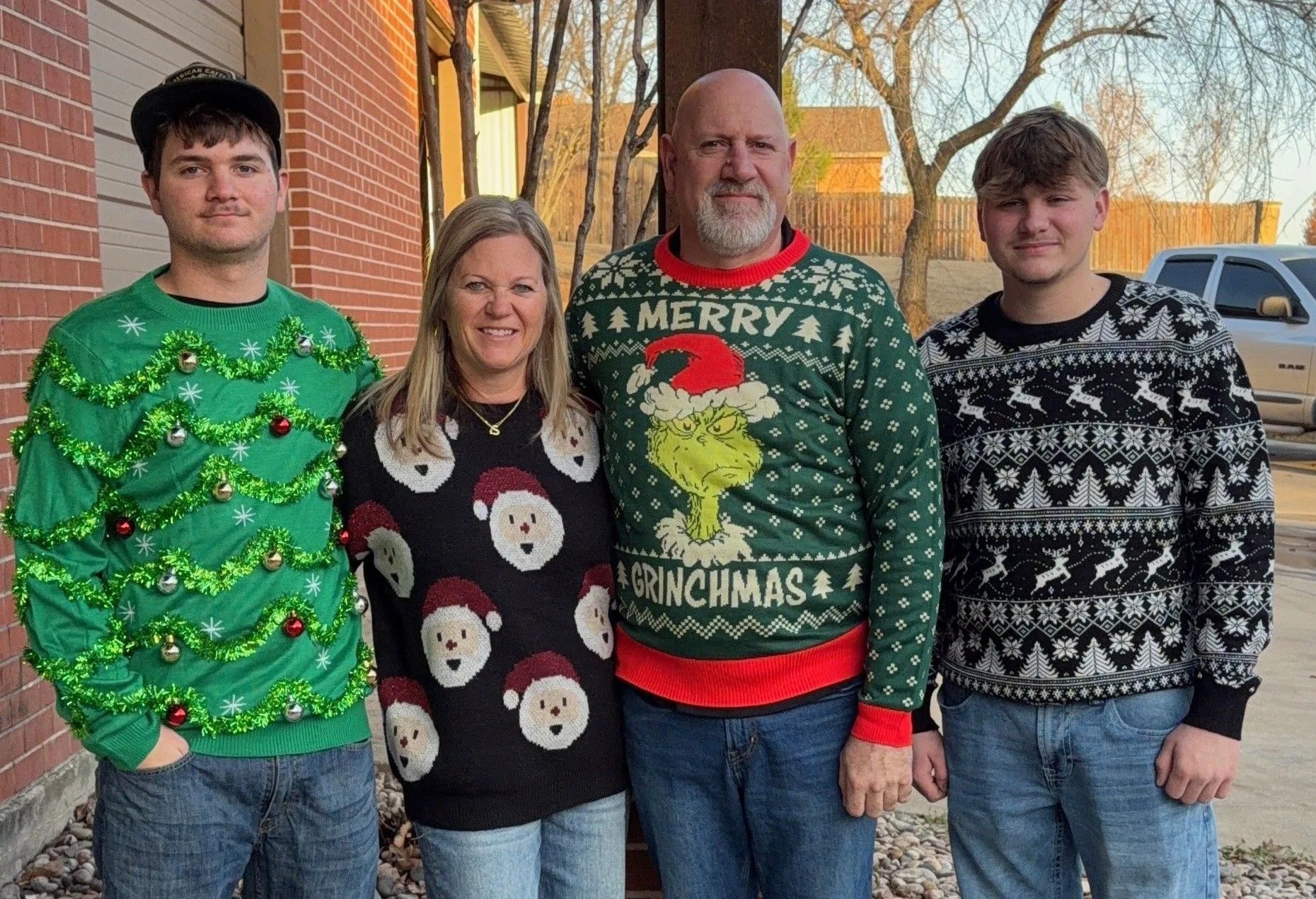 Four smiling people wearing various ugly Christmas sweaters stand outside.