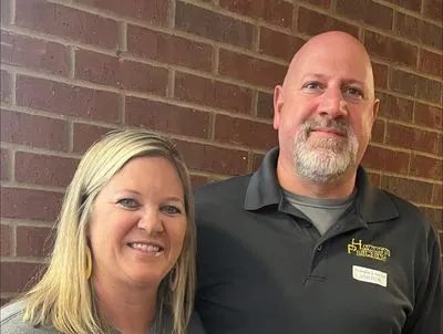 Woman and man, smiling, standing next to each other in front of a brick wall. Both have name tags.
