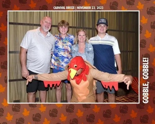 Group photo at Carnival Cruise event: four people and a person in a turkey costume posing with a fall-themed frame.