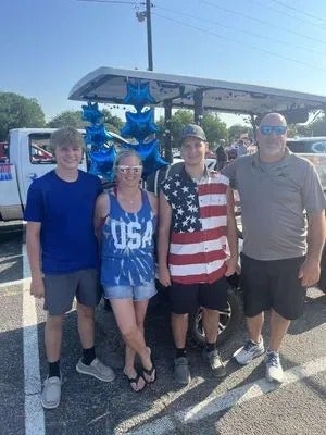 Family poses with decorated golf cart, blue and red patriotic theme.