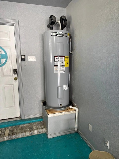 A gray water heater stands on a raised platform next to a white door, with blue flooring.