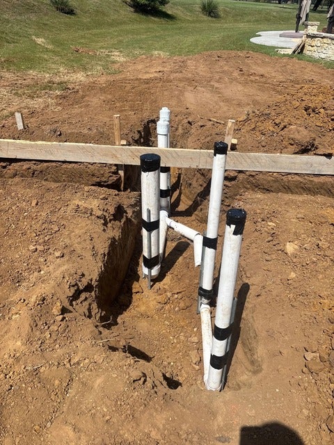 PVC pipes, secured with black tape and partially buried in a dirt trench, ready for a new building foundation.