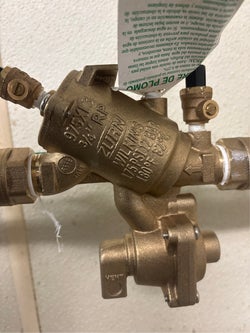 Close-up of a bronze Wilkins backflow preventer valve with connected plumbing and a white tag.