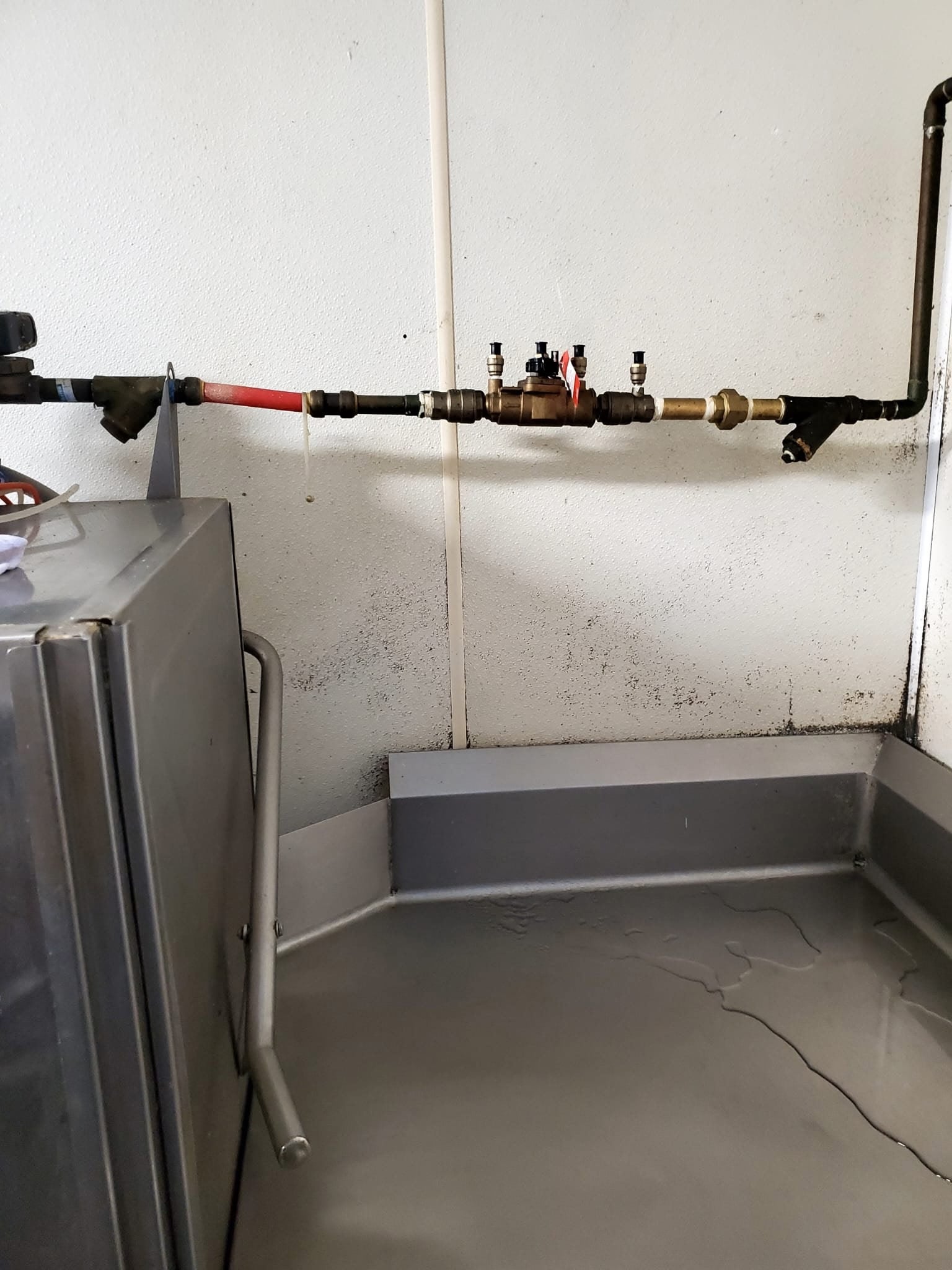 A horizontal pipe system with valves and a red section, above a large gray basin with standing water.