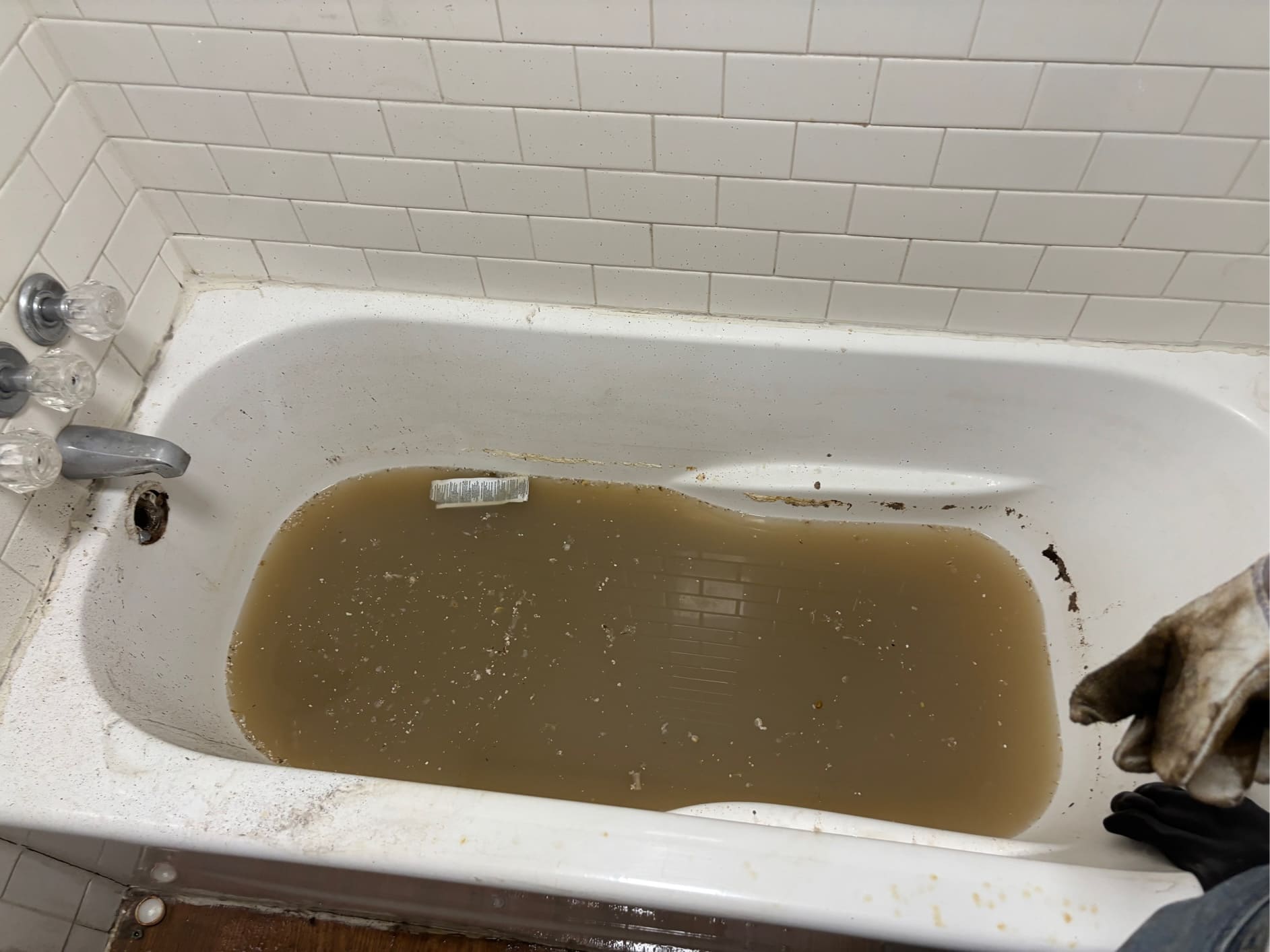 A dirty bathtub filled with murky brown water and unidentified debris, indicating a severe clog or plumbing issue.
