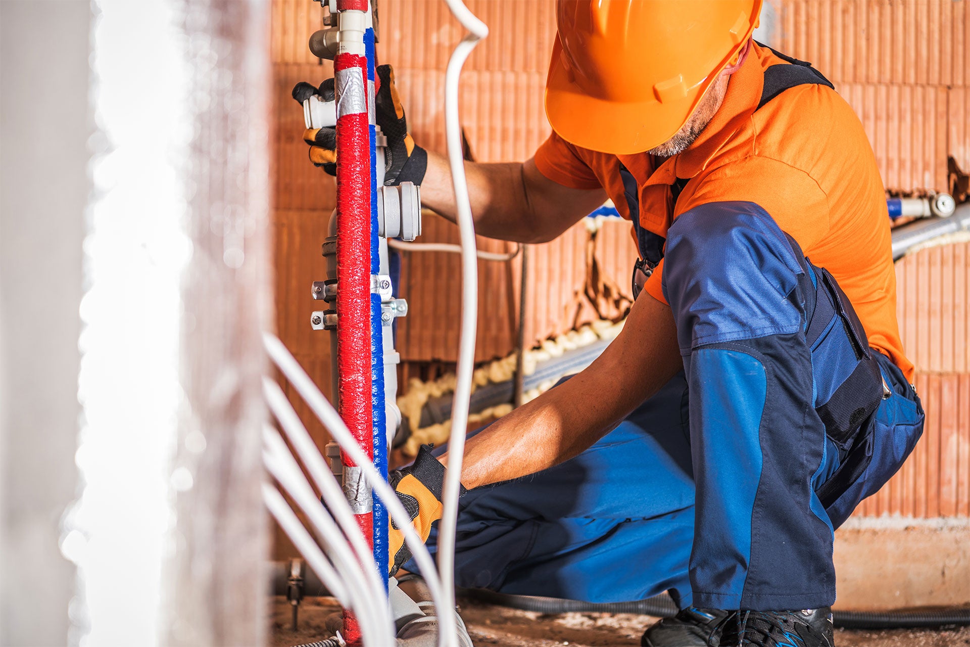 Plumber in a hard hat and work clothes installing hot and cold water pipes.